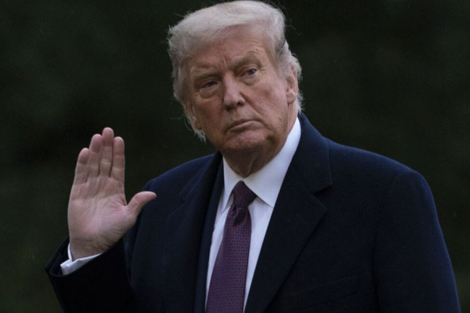 Former President Donald Trump raises his hand while wearing a black coat